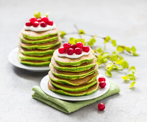 Vegan breakfast, spinach pancakes with cream and cranberries on a plate on a light gray background