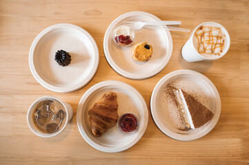 Fototapeta na wymiar Croissant, Banoffee, Scone, Canele on paper plate and iced coffee on wooden table in the cafe
