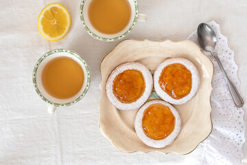 Three homemade baked cookies with citrus jam and two cups of tea. Lemon and spoon on the side.