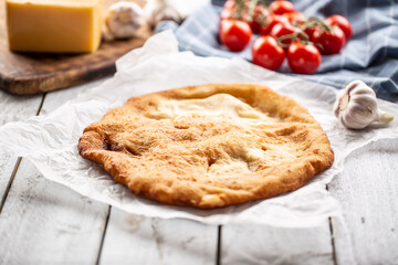 Traditional hungarian dish langos served on a baking paper in the background with garlic tomatoes and cheese on a wooden plate