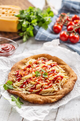 Tasty deep-fried langos served on baking paper with a lot of grated cheese, ketchup and fresh herbs