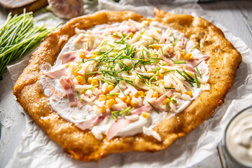 Tasty crusty langos served with sour cream, grated cheese and ham and corn with herbs.