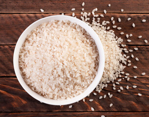 Rice in plate and sprinkled on a wooden background. Top view.