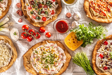 A close up a set of hungarian traditional langos with crusty garlic edges served with vegetables, cream sausages, herbs, grated, cheese, ketchup and dips