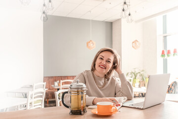 An adult female psychologist coach conducts an online consultation in the bright interior of a cafe with a laptop and a phone on the table. the concept of remote work and psychological assistance.