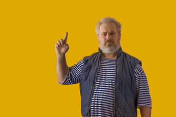 A man with a gray beard, gray hair, wearing a sailor shirt and sleeveless jacket, shows the symbol...
