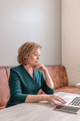 An adult female psychologist coach conducts an online consultation in the bright interior of a cafe with a laptop and a phone on the table. the concept of remote work and psychological assistance.