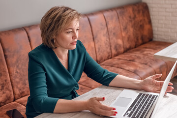 An adult female psychologist coach conducts an online consultation in the bright interior of a cafe...