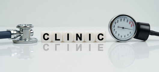 On a reflective white surface lies a stethoscope and cubes with the inscription - CLINIC