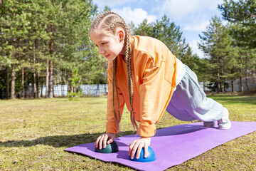 A teenage girl goes in for sports in nature, on a sunny summer day she does push-ups on a sports mat. Healthy lifestyle. Outdoor workout. Exercises for correct posture, healthy back.