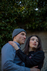 A couple of love guy in a gray hat and blue shirt and brunette girl with big eyes hug each other and look to the side. High quality photo