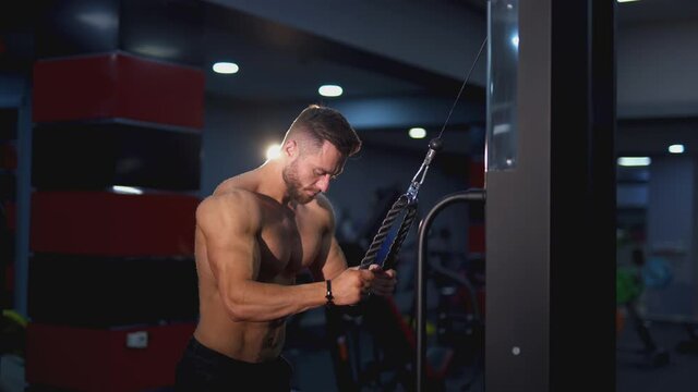 Athletic guy pumping his muscles. Shirtless bodybuilder training his sportive body in the gym. Side view. Sportive lifestyle.