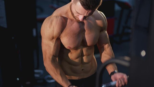 Training muscles. Sportsman pumping his trained body on a simulator. Strong trainer doing workout. Exercise to improve strength at fitness club. Close-up.