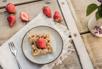 Piece of rhubarb crumble cake and strawberries on a plate on an old wooden table