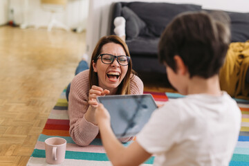 mother and son having fun at home. boy using digital tablet