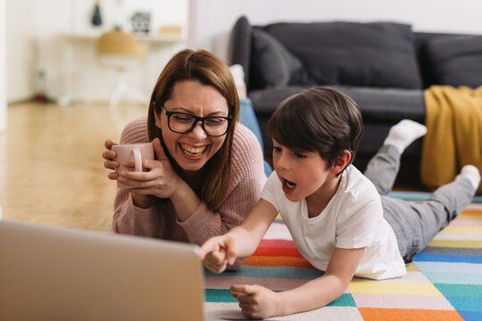 Mother And Child Laying On Floor And Using Laptop Computer At Home