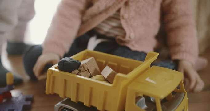 Boys toys on the floor of living room, View of childs hands putting Construction Materials to a plastic yellow van, wooden bricks and plasticine. Kids leisure activity. Entertainment for children