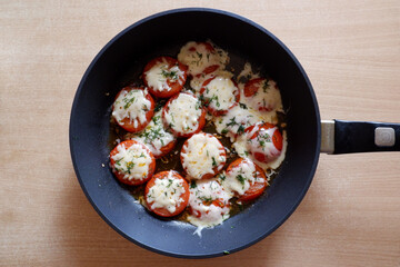 Tomatoes baked with cheese in a frying pan on the table. Cook at home 