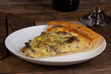 One slice or piece of pizza of meat or rump or filet, on a white plate, on a wooden table, next to a glass and bottle of wine