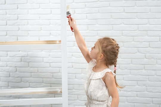 Close up of girl in white shirt holding brush and painting rack in white color. Concept of process painting rack at home.