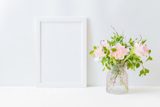 Mockup with a white frame, pink tulips and branches with green leaves in a vase on a light background