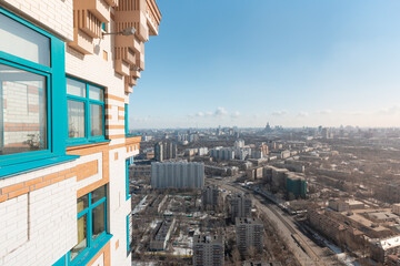 Close up view of an external wall and windows of a residential house and aerial view of residential areas of a large city with multi-storey buildings against a blue sky with light clouds