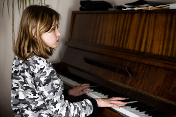 At home, a young girl plays the piano and looks away, she checks herself or knows a piece of music by heart. The girl is preparing for the music exam at school