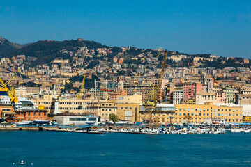 Naklejka premium Scenic view of the maritime city of Genoa in Italy. View from the sea to the Italian city of Genoa, beautiful colorful houses along the coast, harbor cranes and yachts moored at the pier.