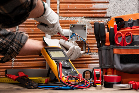 Electrician worker with a screwdriver fixes the cable in the terminal of the switch of an electrical system. Working safely with protective gloves. Construction industry. 