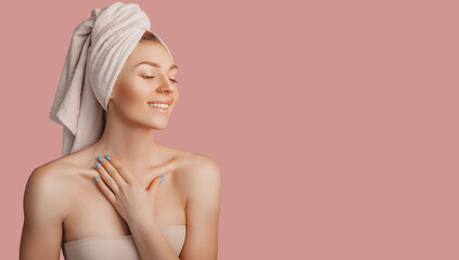 Beautiful sensual young girl with clean skin on a pink background with a mockup. Topless woman in a towel. The concept of spa treatments, natural beauty and care, youth, cream and mask, freshness