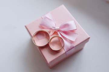 Top view of beautiful new pair of elegant gold wedding rings, placed on the top of pink square ring box, lace on the white background
