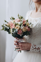 Young bride in wedding lace dress holding bouquet with pink and biege roses and green eucaliptus, studio shot.