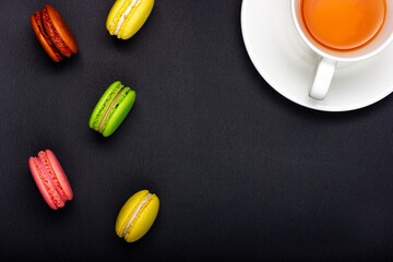 Colored macaroon cookies and a cup of tea on a black background.