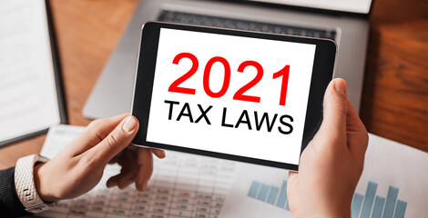 Man hands holding tablet with text 2021 tax laws at workplace. Businessman working at desk with documents