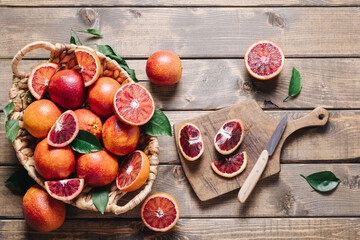 Whole and sliced blood oranges with knife and chopping board over wooden table background. Summer...