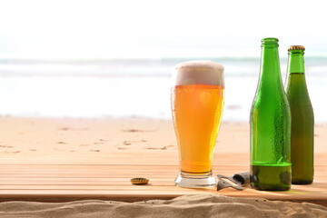 Glass of beer and two bottles on wood in sand
