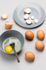 Broken egg and fork in gray bowl. Chicken shells on gray plate. Brown eggs on table