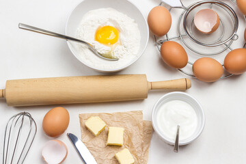 Rolling pin for dough. Broken egg and flour in bowl.