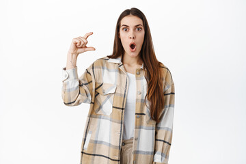Surprised and impressed woman holding small little thing, hand tiny object gesture over copy space,...