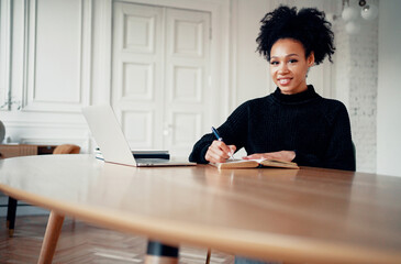 Freelancer remote communication with colleagues. Designer student female afro appearance. Works at home online makes a new project on a laptop. Clothing for working in a coworking space.