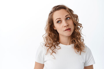 Cute silly woman biting lip and look thoughtful aside, dreaming or wanting something, daydreaming, standing over white background