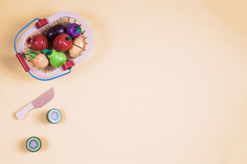 Wooden toy fruits and vegetables in the basket on pastel background. Healthy food. Top view