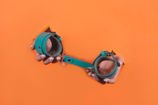 Adult sex toys, minimal design, isolated on an orange background. Women's hands in handcuffs