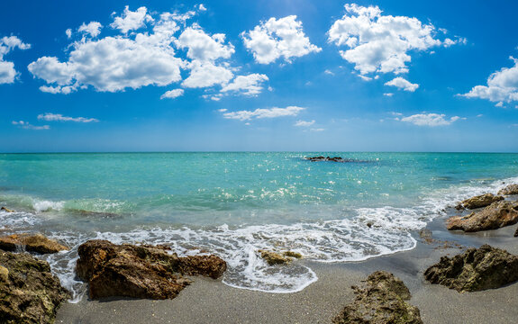 Small waves breaking amoung rocks on the shore of the Gilf of Mexico at Caspersen Beach with blue sky and white clouds in Venice Florida USA