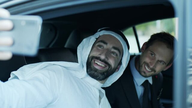 The sheik and the businessman take a selfie in the car.
