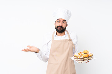 Young man holding muffin cake over isolated white background having doubts while raising hands