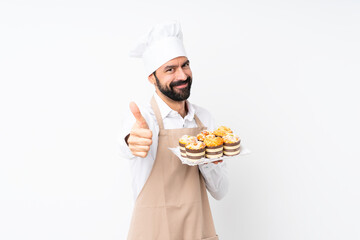 Young man holding muffin cake over isolated white background with thumbs up because something good has happened