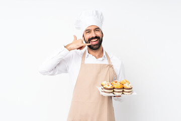 Young man holding muffin cake over isolated white background making phone gesture. Call me back sign
