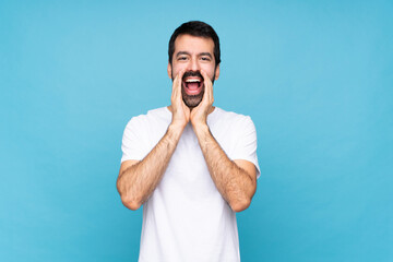 Young man with beard  over isolated blue background shouting and announcing something