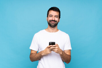 Young man with beard  over isolated blue background sending a message with the mobile